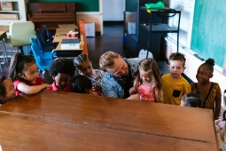 A teacher interacts with children in a bright classroom filled with educational materials and colorful decorations.