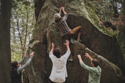 four youth near a walk helping one of the attempting to climb it