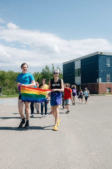 The image shows students holding a pride flag in a school playground.