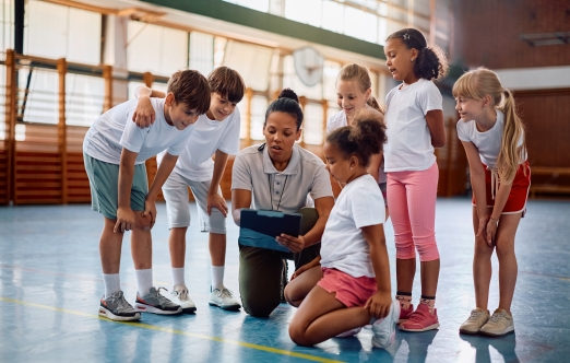 A teacher engages with a group of children in a gym setting, fostering interaction and learning.