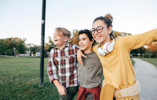 A group of three school-age children can be seen walking together outside a school. They appear happy and are clearly enjoying each other's company.