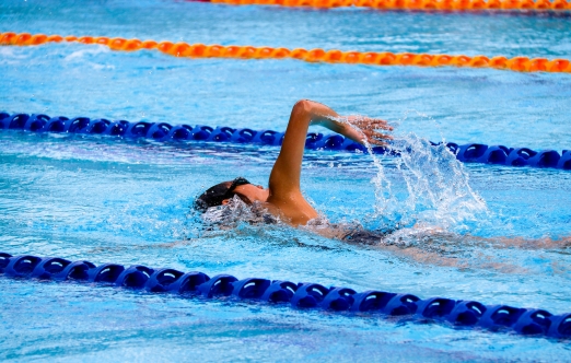 A person swimming in a clear blue pool, creating ripples in the water.