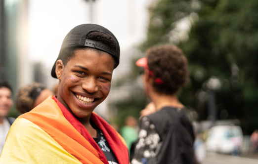 A young person carrying a rainbow flag and flashing an contagious, confident smile.